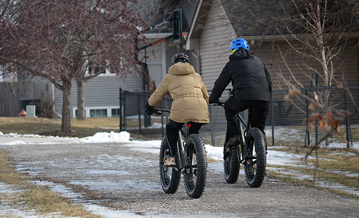 Two fat-tire bike riders head away on a gravel path in winter.