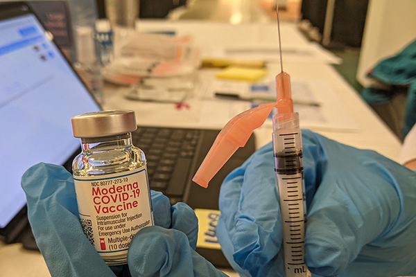 Gloved hands display a vile of Moderna's COVID-19 vaccine and a syringe