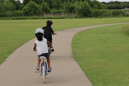 Children ride bikes on a bike path with trees in the distance.