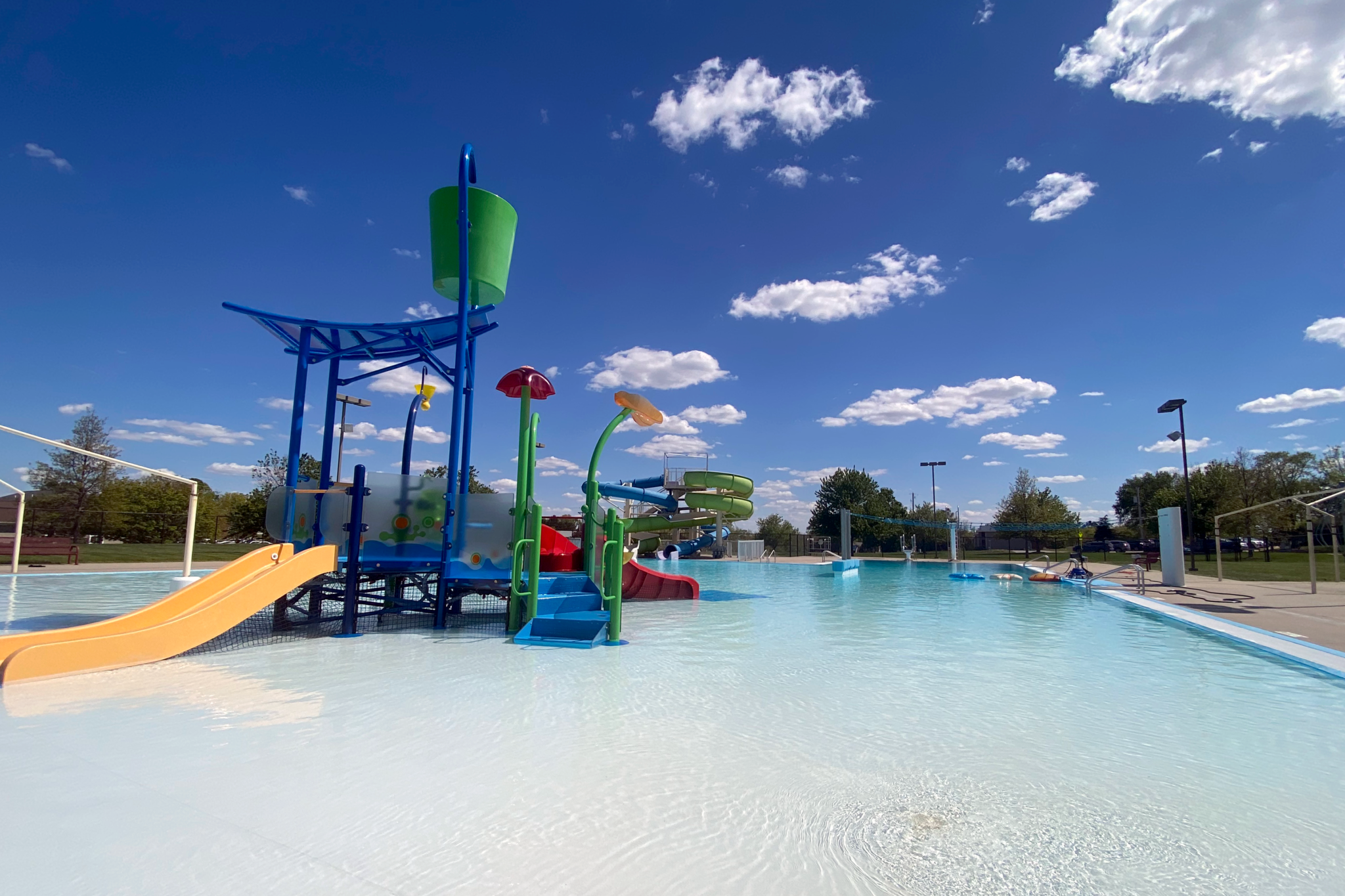 A wide-angle photo of the North Liberty outdoor pool under clouds and blue sky