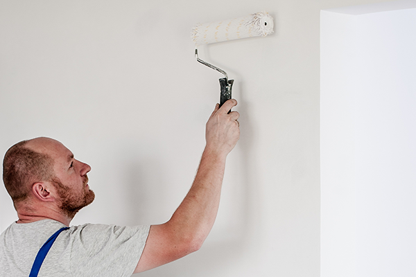 A man paints a house wall with a roller.