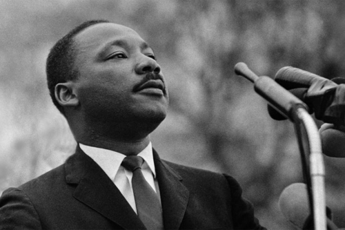 Martin Luther King Jr is pictured standing in front of a pair of microphones