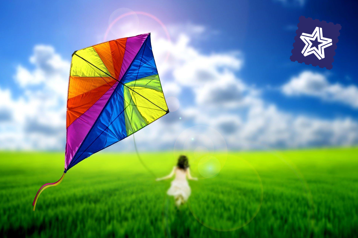 A child flies a brightly diamond colored kite over bright green grass with clouds and blue sky.