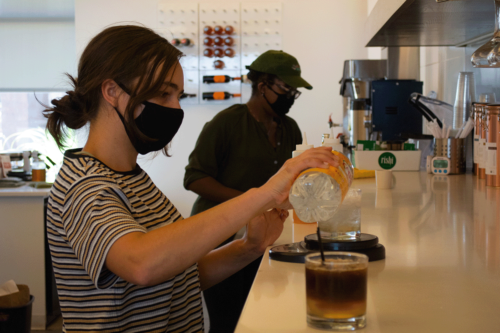 Two employees, wearing masks, make coffee drinks during the Covid-19 pandemic.