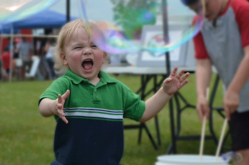 A child runs through a park after a very large soap bubble.