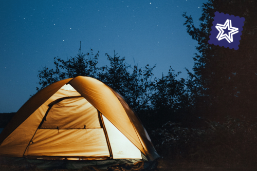 A glowing tent pitched under the stars among silhouetted trees.