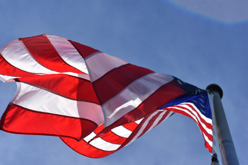 The flag of the United States of American flies against a blue sky.