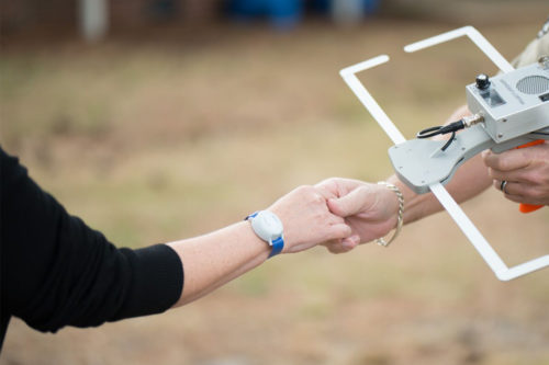 A person wearing a Project Lifesaver transmitter on their wrist holds hands with a law enforcement agent holding a tracking device.