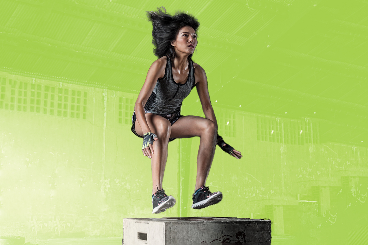 A woman working out by doing box jumps in a gritty gym setting.