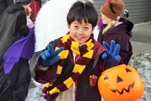 A child dressed as Harry Potter and a coat and gloves trick or treats in winter.