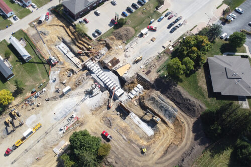 An aerial photo of a construction site. In the center of the frame, the roadway has been removed and a concrete tunnel has been pieced together in middle of the roadway. Dirt has been excavated at both ends of the tunnel.