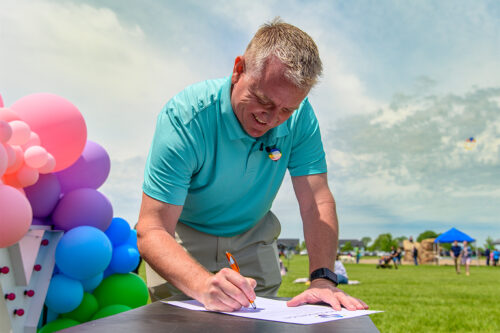 Mayor Chris Hoffman smiles as he signs a proclamation for Pride Month at an outdoor event
