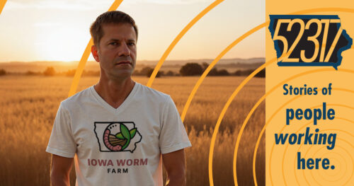 adam schechinger state farm agent and founder of the iowa worm farm standing in an undisclosed location - a farm field it would appear - wearing an iowa worm farm shirt and looking quite serious.